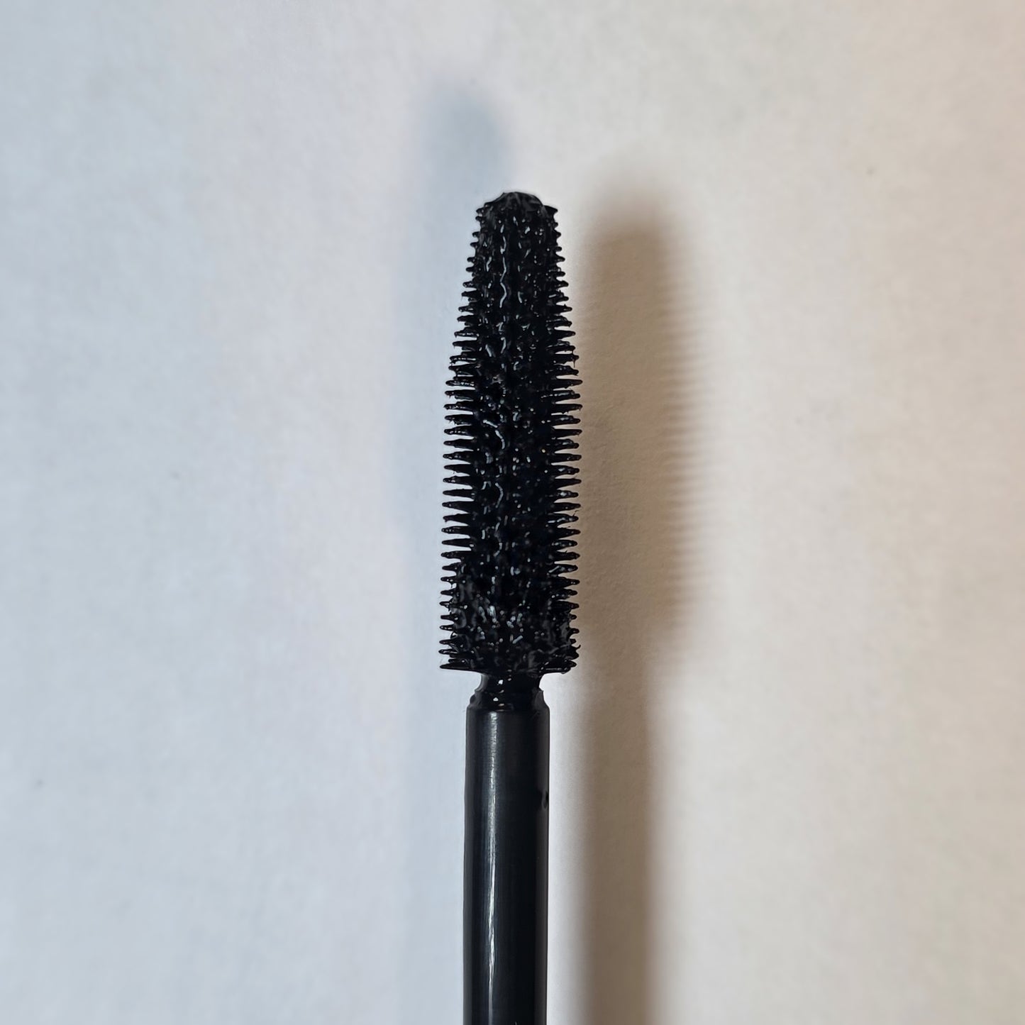Black mascara wand on a light gray background