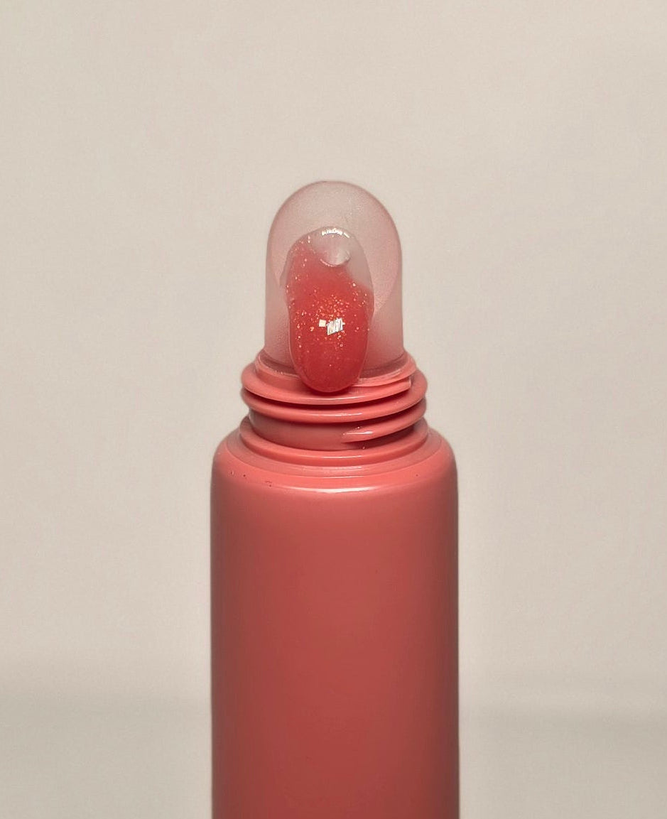 Pink lip gloss tube with clear cap on a beige background