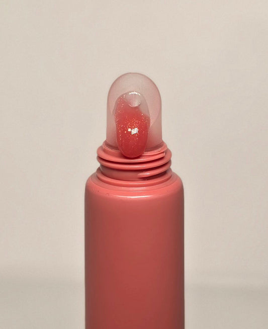 Pink lip gloss tube with clear cap on a beige background
