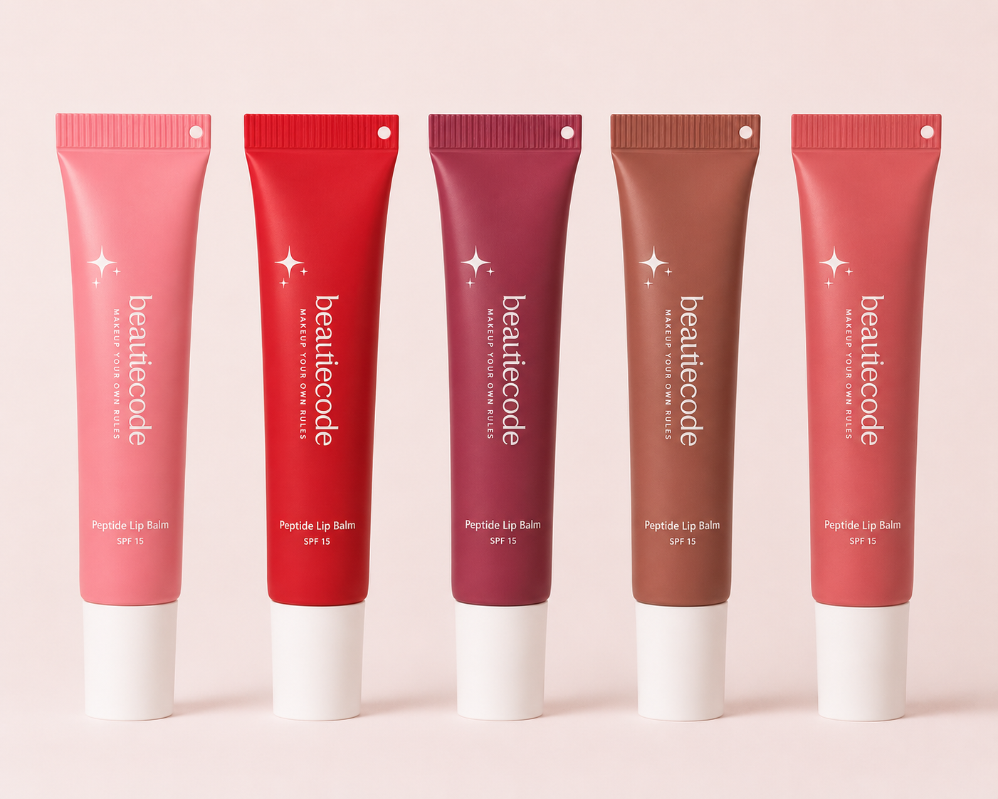 Five beautiecode Peptides Lip Balm tubes in different shades of pink, red, mauve, brown, and coral, arranged in a row against a solid pale pink background.