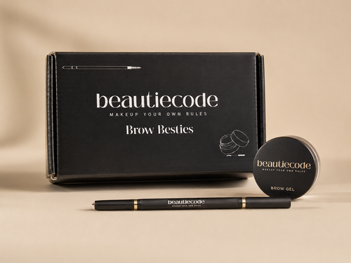 Beautiecode Brow Besties makeup kit featuring a black box, a black brow gel jar, and a black brow pencil with gold accents, arranged on a beige background.