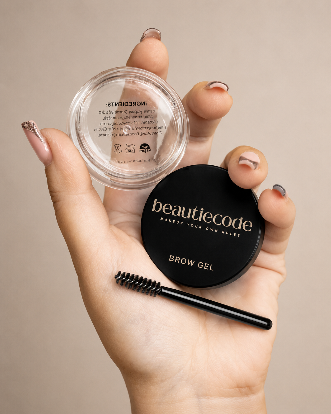 pot of beautiecode brow gel being held with the spoolie by a nicely manicured hand