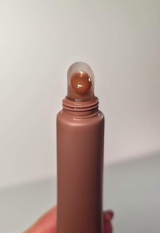 Brown colored lip gloss with a clear cap on a light gray background