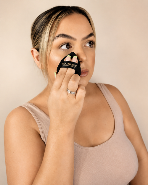 woman holding small black powder puff to face to set makeup with beautiecode logo on it