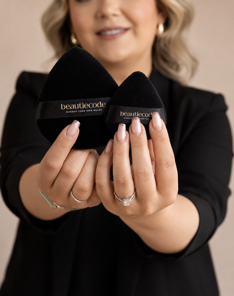 a beauty lover holding a small and large black powder puff in each hand with the beautiecode logos on them