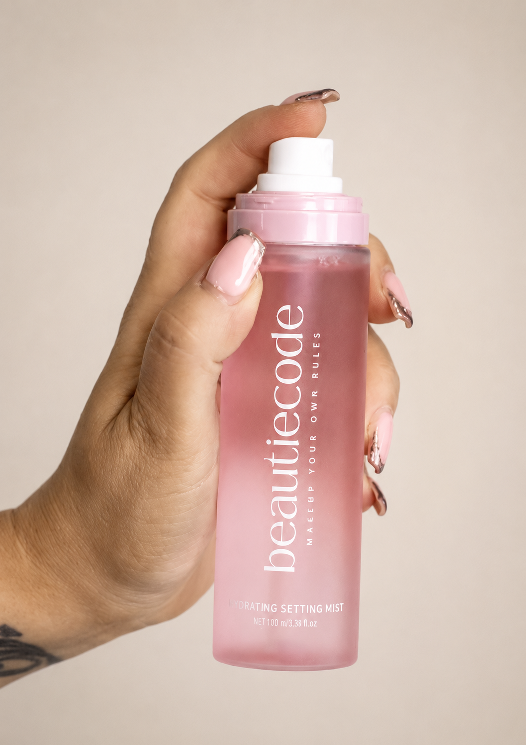 pink bottle of beautiecode hydrating setting mist being sprayed by a hand with perfectly manicured nails