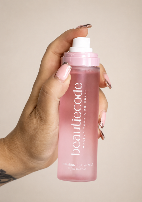 pink bottle of beautiecode hydrating setting mist being sprayed by a hand with perfectly manicured nails