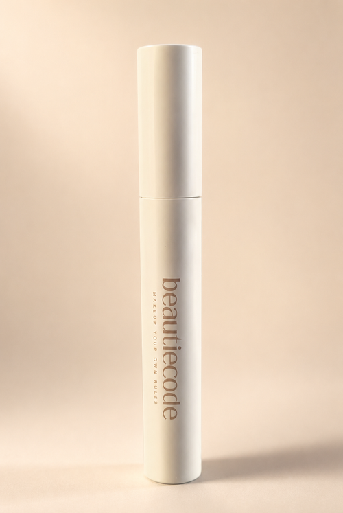 A tall, slim white cosmetic bottle with the brand name 'beautiecode' printed vertically in a muted taupe-brown font, set against a solid, warm beige background.